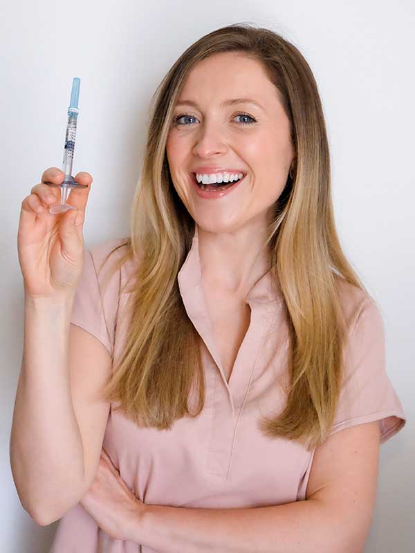 Kelsey-600×800-TreatmentHero Nurse Kelsey smiling and holding a needle